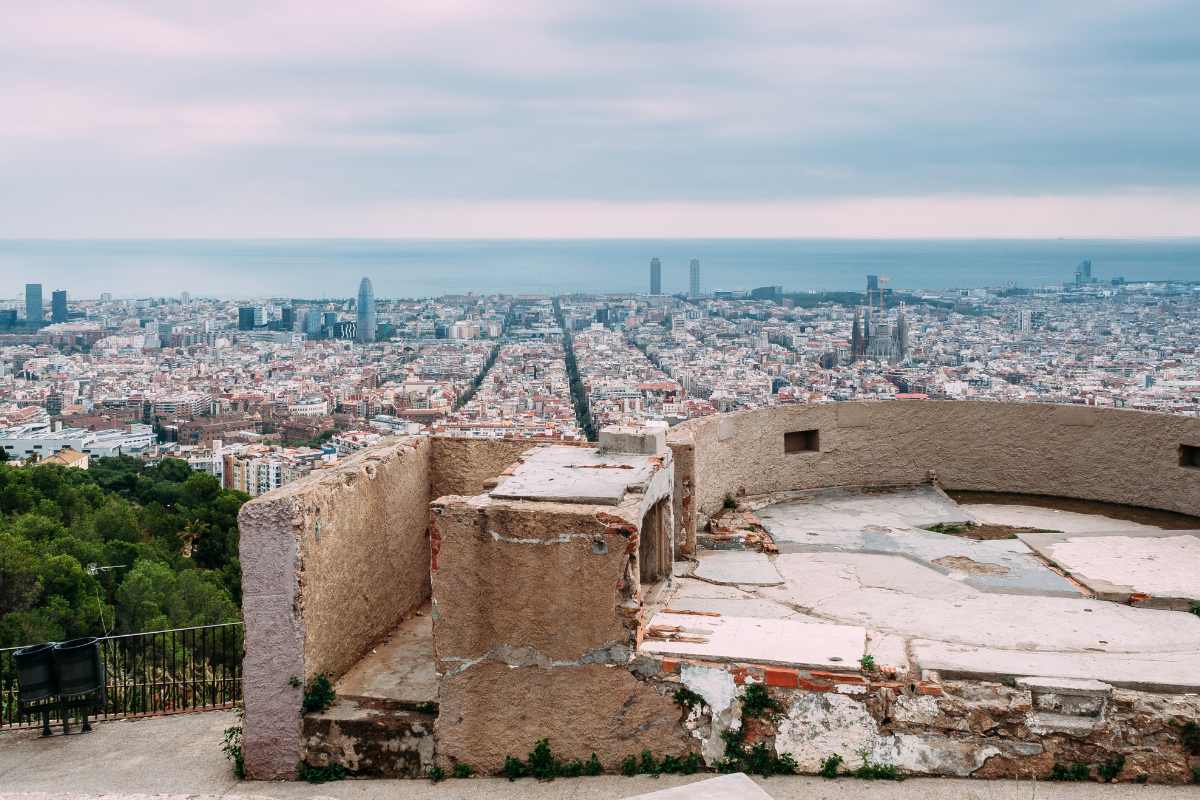 Elevated view of Barcelona cityscape on an overcast day, seen from the vantage point of Bunkers del Carmel with ancient stone walls in the foreground