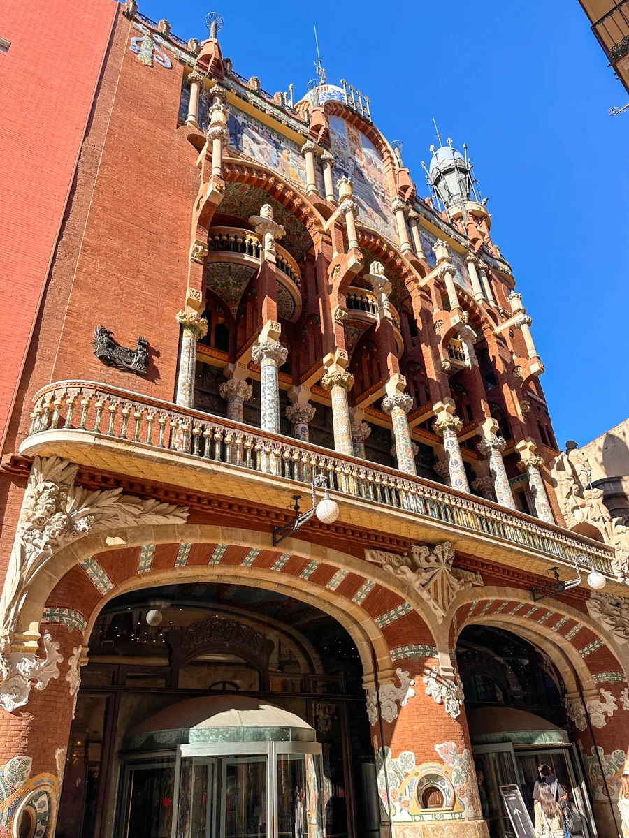 The ornate facade of Palau de la Música Catalana, adorned with intricate mosaics, floral sculptures, and colorful columns under a blue sky.