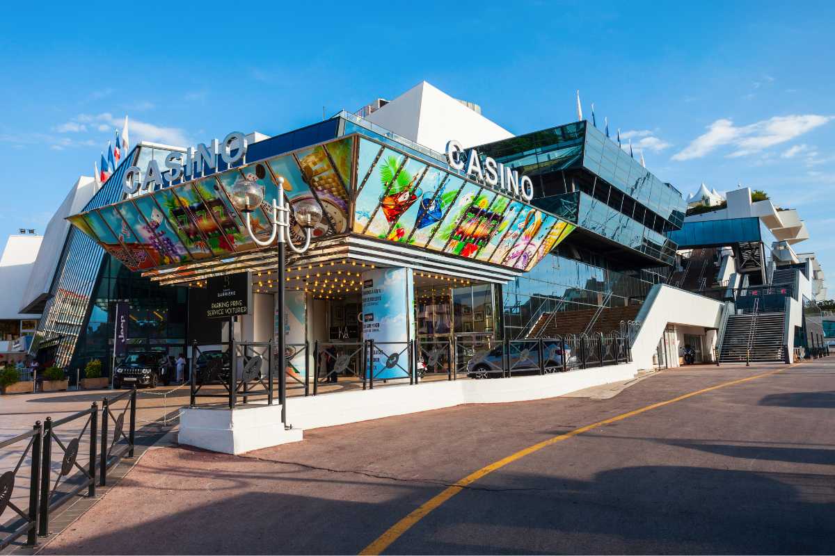 The modern facade of the Casino Barrire in Cannes, featuring a vibrant, artistic entrance, with a clear sky above and a quiet esplanade in front.