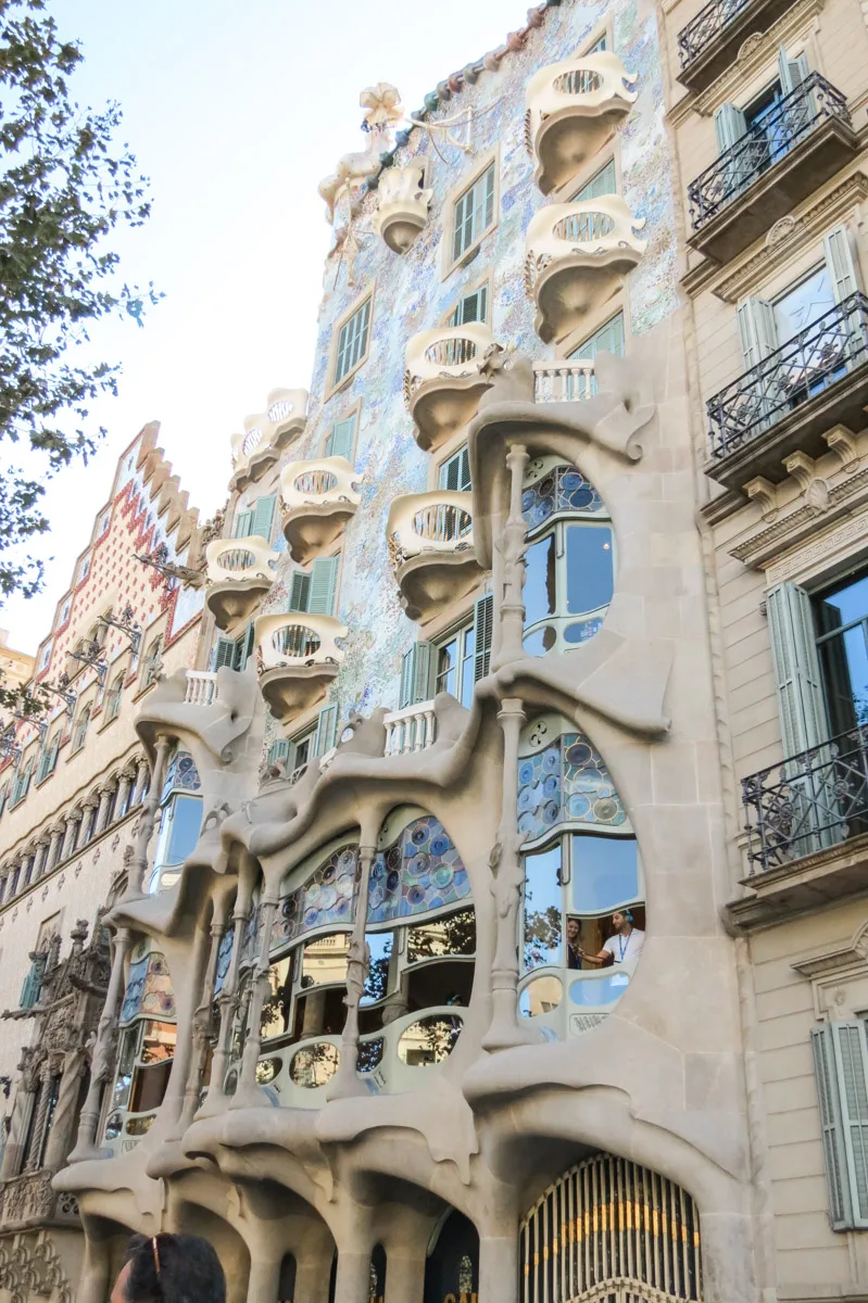 Exterior of Casa Milà (La Pedrera), showcasing its unique undulating stone facade and wrought-iron balconies, against the backdrop of a clear blue sky.