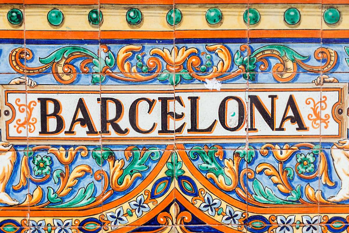 Close-up of colorful, ornately patterned ceramic tiles spelling 'BARCELONA' with decorative motifs in green, blue, and orange. A street art tour is a great thing to do in Barcelona alone.