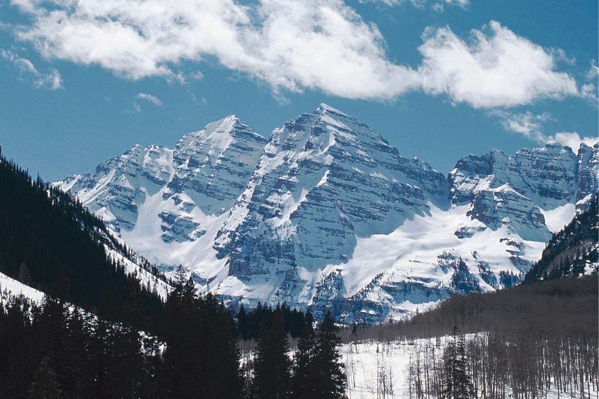 The Maroon Bells mountains tower majestically over the surrounding forest under a clear blue sky in Aspen
