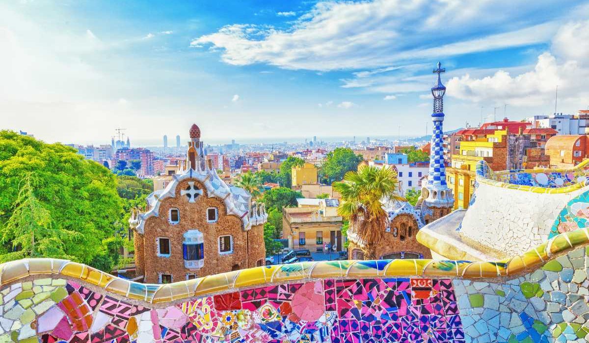 stunning picture of a colorful bench at parc guell in barcelona with the cityscape in the background. this is one of the must do things when in barcelona on a cruise