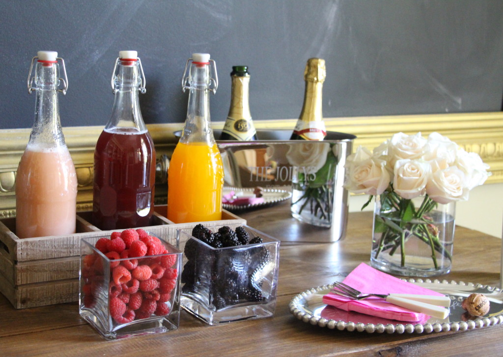 Chalkboard mimosa bar sign with orange and white flowers, champagne glasses, fruit, juice and champagne