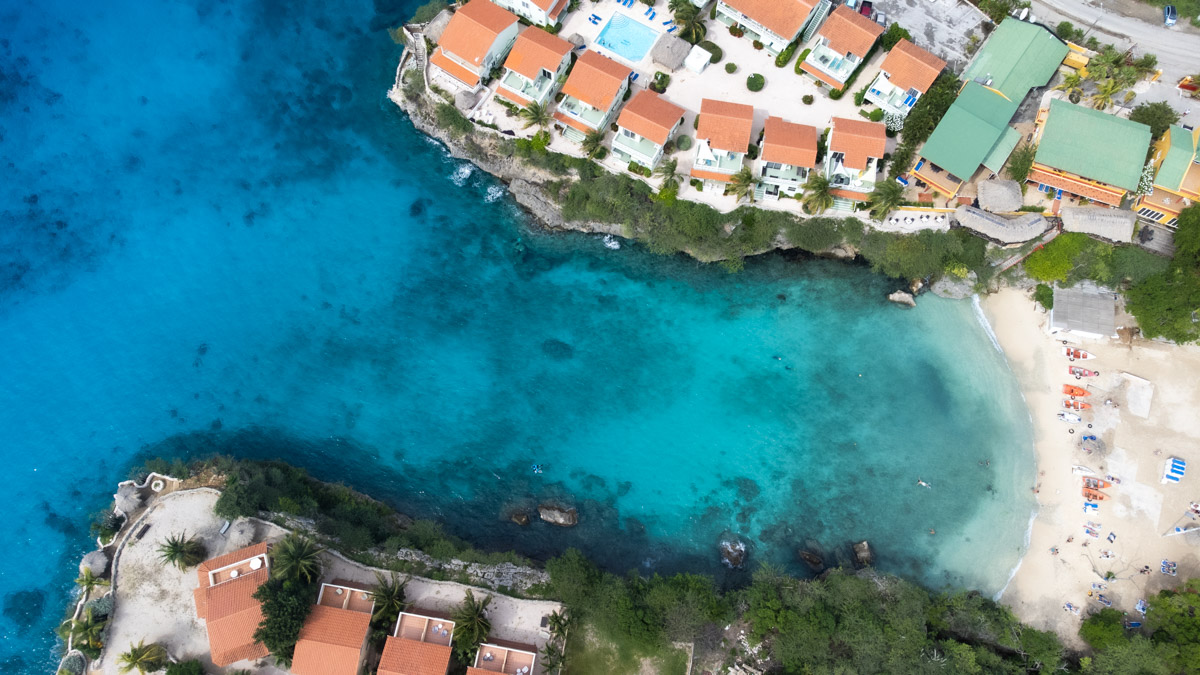 Aerial view of Playa Lagun, Curacao showing a bustling beach nestled between rugged cliffs and turquoise waters