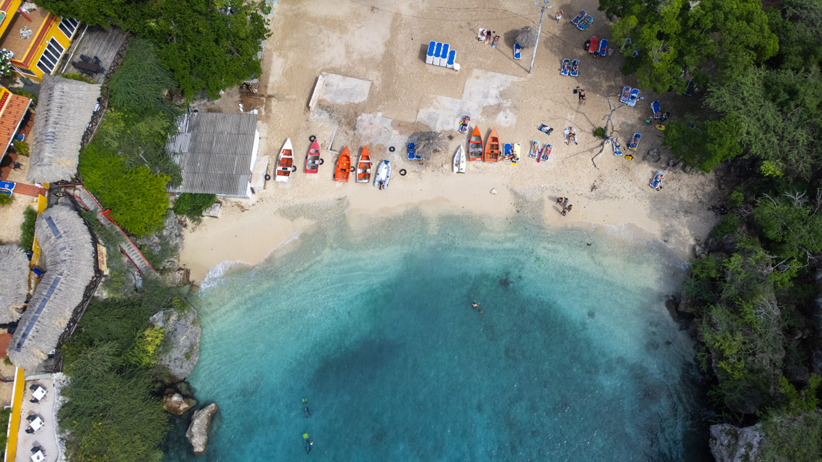 Top view of a busy beach day at Playa Lagun, Curacao, with kayaks and snorkelers enjoying the clear, shallow waters