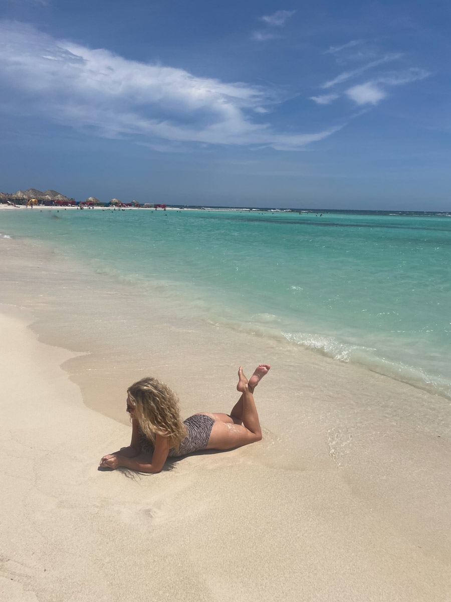 Woman sunbathing on a pristine white sand beach with clear blue waters under a partly cloudy sky.